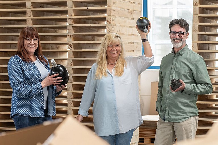 Drei Mitarbeiter halten jeweils ein Produkt von Hennlich HCT: Ersatzblase, Membranspeicher und Absperrblock