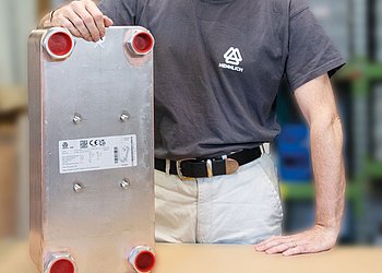 Auf einem Tisch steht ein Plattenwärmetauscher, dahinter steht ein Mitarbeiter in Hennlich Shirt