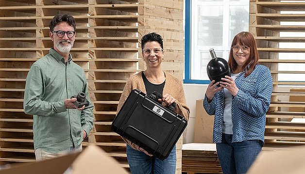 Drei Mitarbeiter halten jeweils ein Speicherzubehörteil: Sicherheits- und Absperrblock, Füllprüfkoffer und Ersatzblase