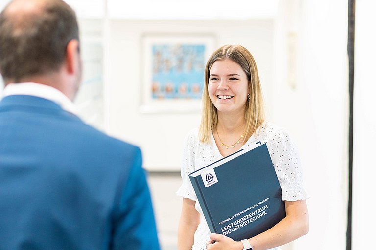 Neue Mitarbeiterin mit Infomaterial wird von ihrem neuen Vorgesetzten begrüßt