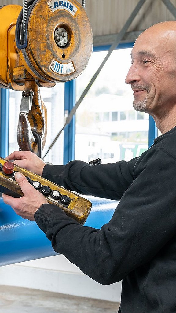 Mitarbeiter transportiert einen langen Blasenspeicher mittels Elektrokettenzug