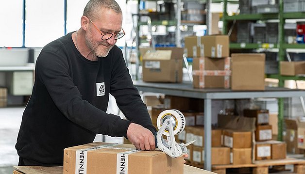 Michel Berlocker verpackt eine Bestellung für einen Kunden mit Hennlich Packband